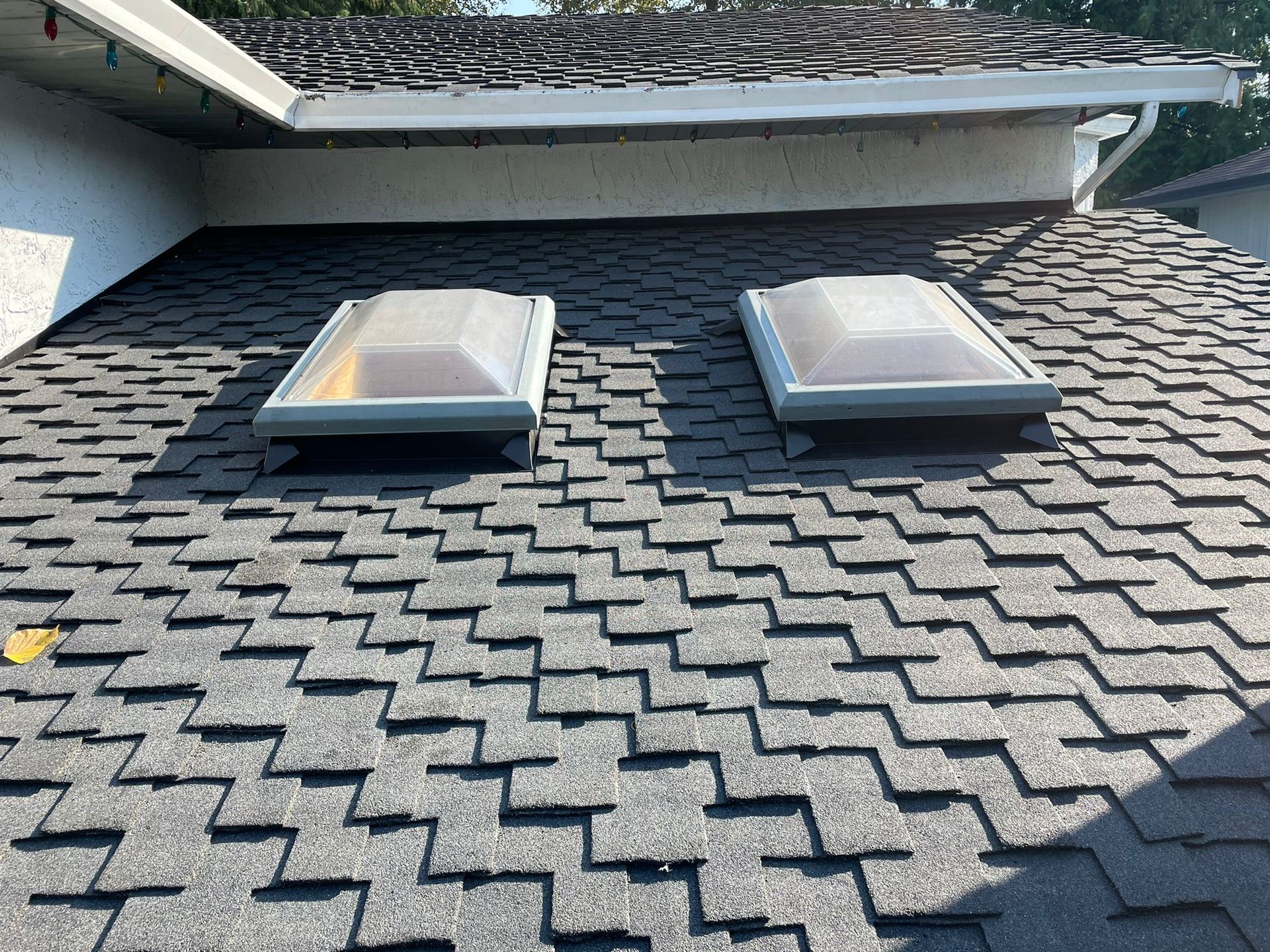 Close-up of a weathered cedar shake roof under a clear blue sky with a dome skylight.