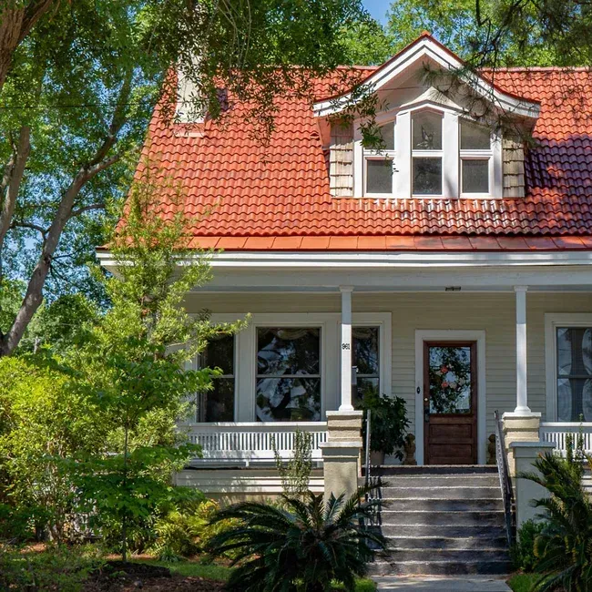 Beige house with red tile roof, porch, and dormer under a sunny sky.