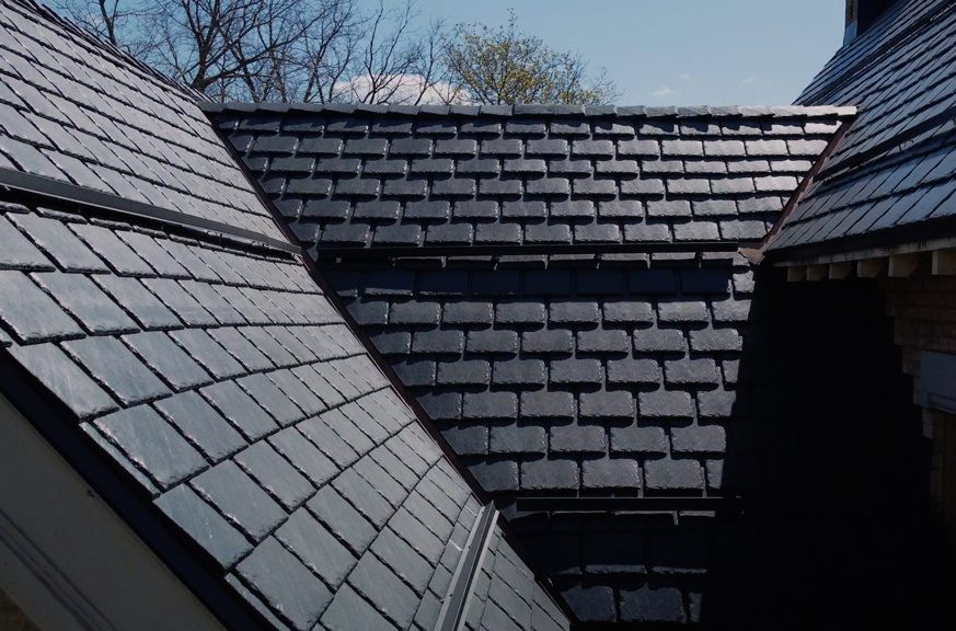 A roof with a vent on it and a building in the background.