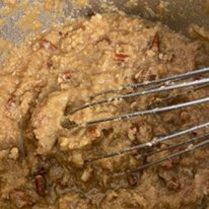 Oatmeal mixture with pecans being whisked in a metal bowl.