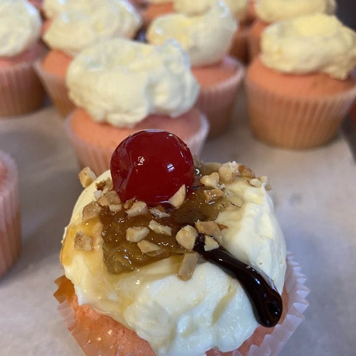 Pink cupcakes topped with cream, nuts, cherry, and syrup.