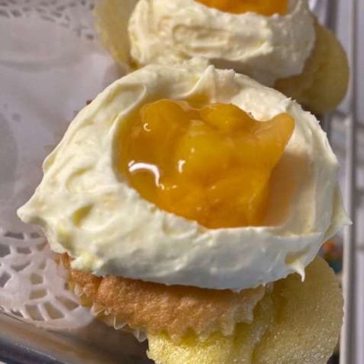 Cupcake with white frosting and peach filling on a lace doily.