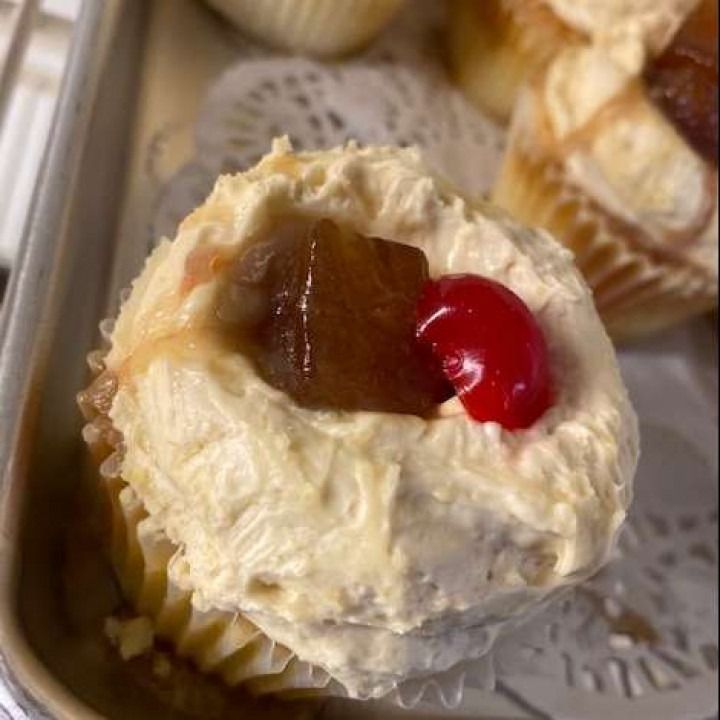 Cupcake with frosting, a cherry, and a candied piece, on a tray.