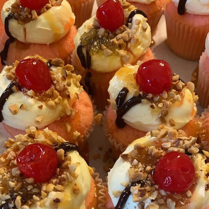 Cupcakes with cream frosting, cherries, nuts, and chocolate drizzle.