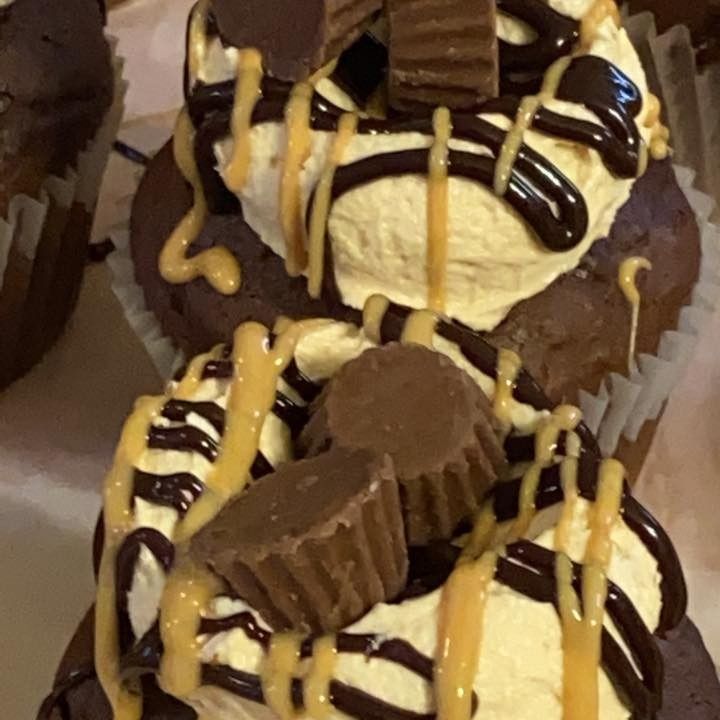 Chocolate cupcakes with peanut butter frosting, drizzled with chocolate and peanut butter, topped with Reese's cups.
