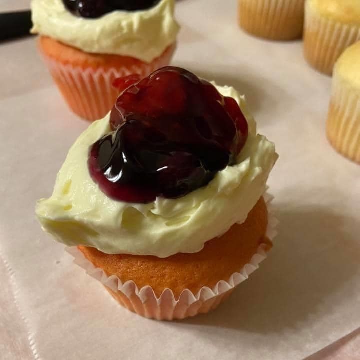 Cupcake with orange base, cream frosting, and cherry topping.