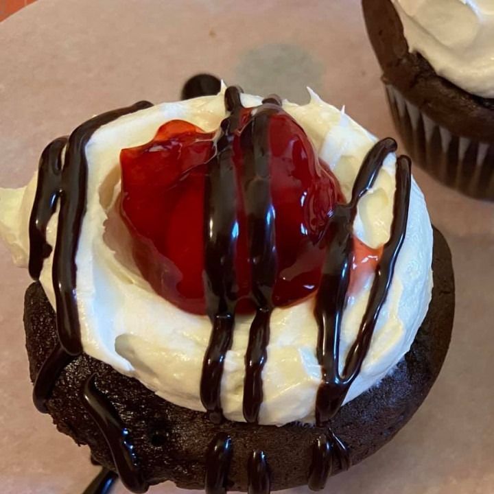 Chocolate cupcake with white frosting, a cherry, and chocolate drizzle.