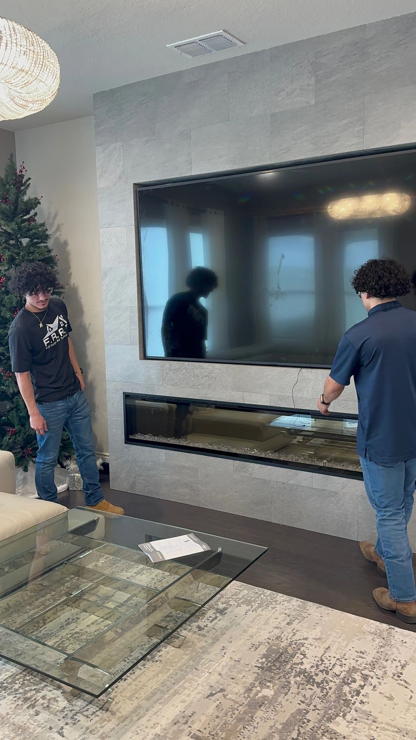 Two men install a large wall-mounted TV in a modern living room.