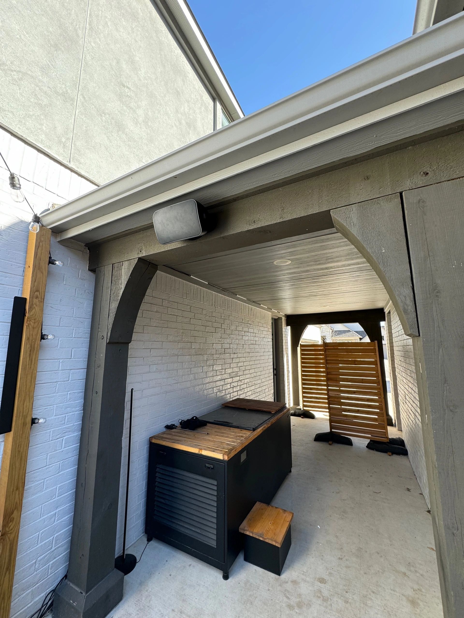 Narrow covered outdoor passage with white walls, a storage box, and sunlight at the far end.