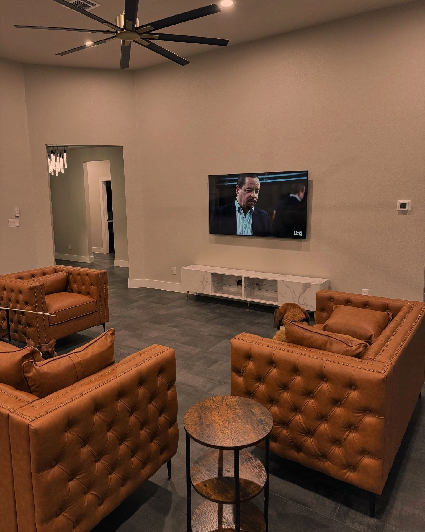 Modern lounge with tan tufted chairs facing a wall-mounted TV and beige walls.