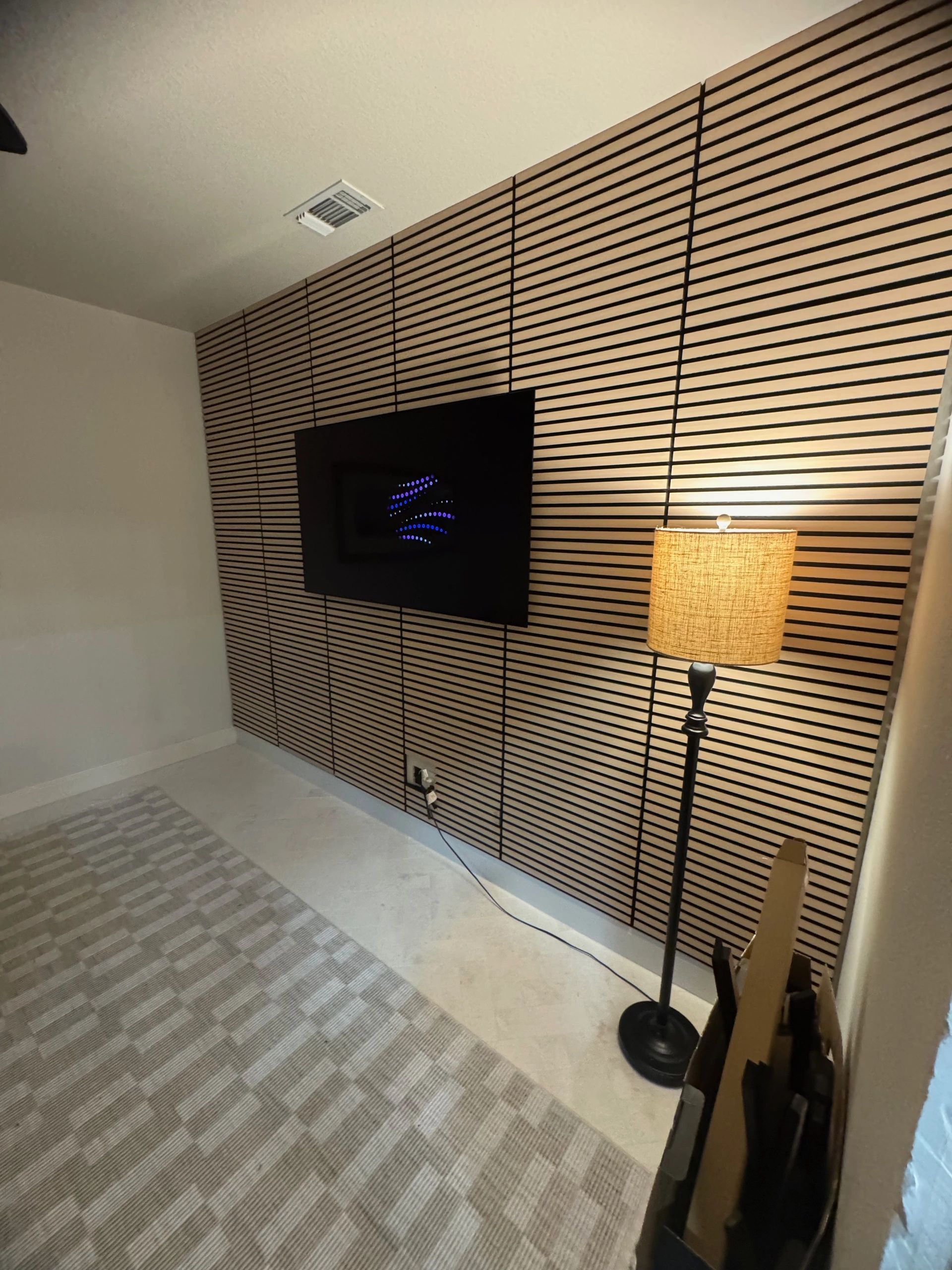 Living room with a wall-mounted TV on a wood slat accent wall and a floor lamp on the right.