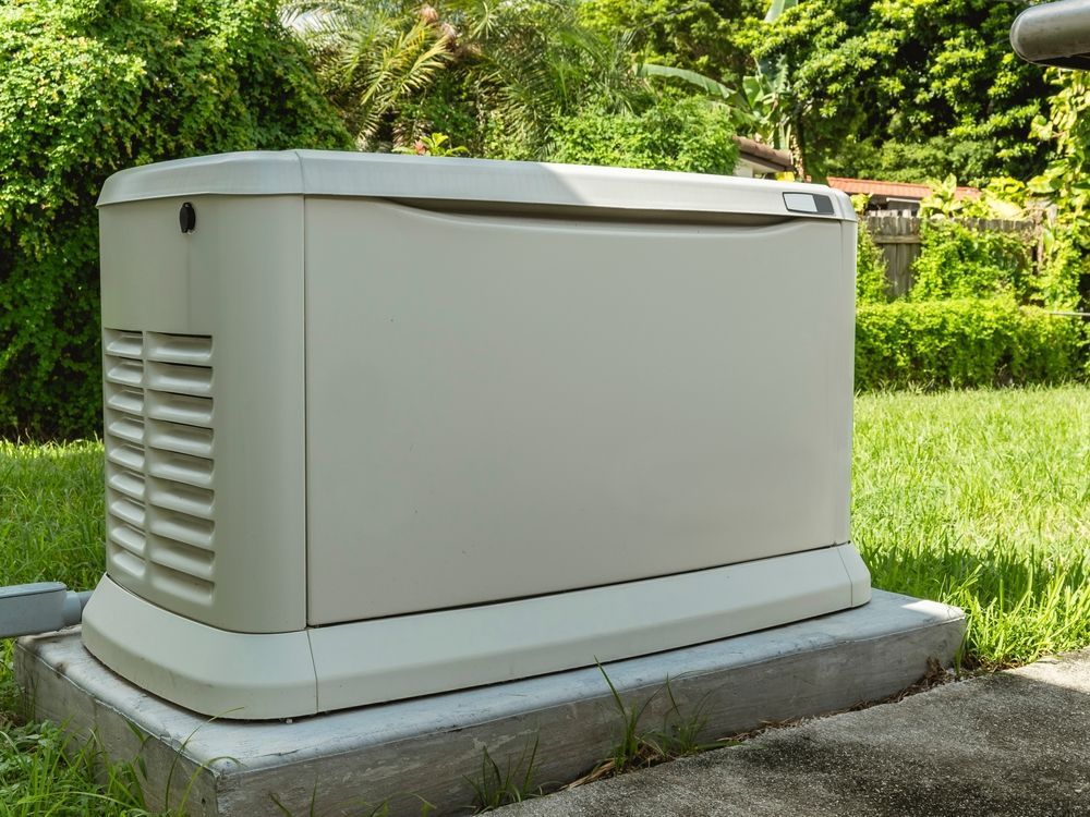A beige home generator on a concrete base in a grassy yard, surrounded by greenery.