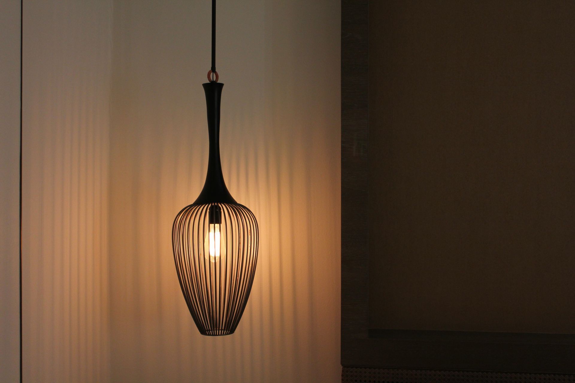 Black pendant lamp with a wood-like patterned shade, casting light on a wall.