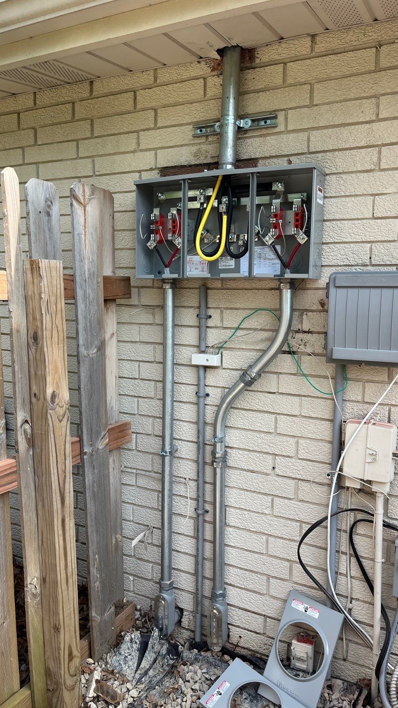 Electrical panel mounted on a brick wall with conduits and wiring visible. Gray and yellow components.