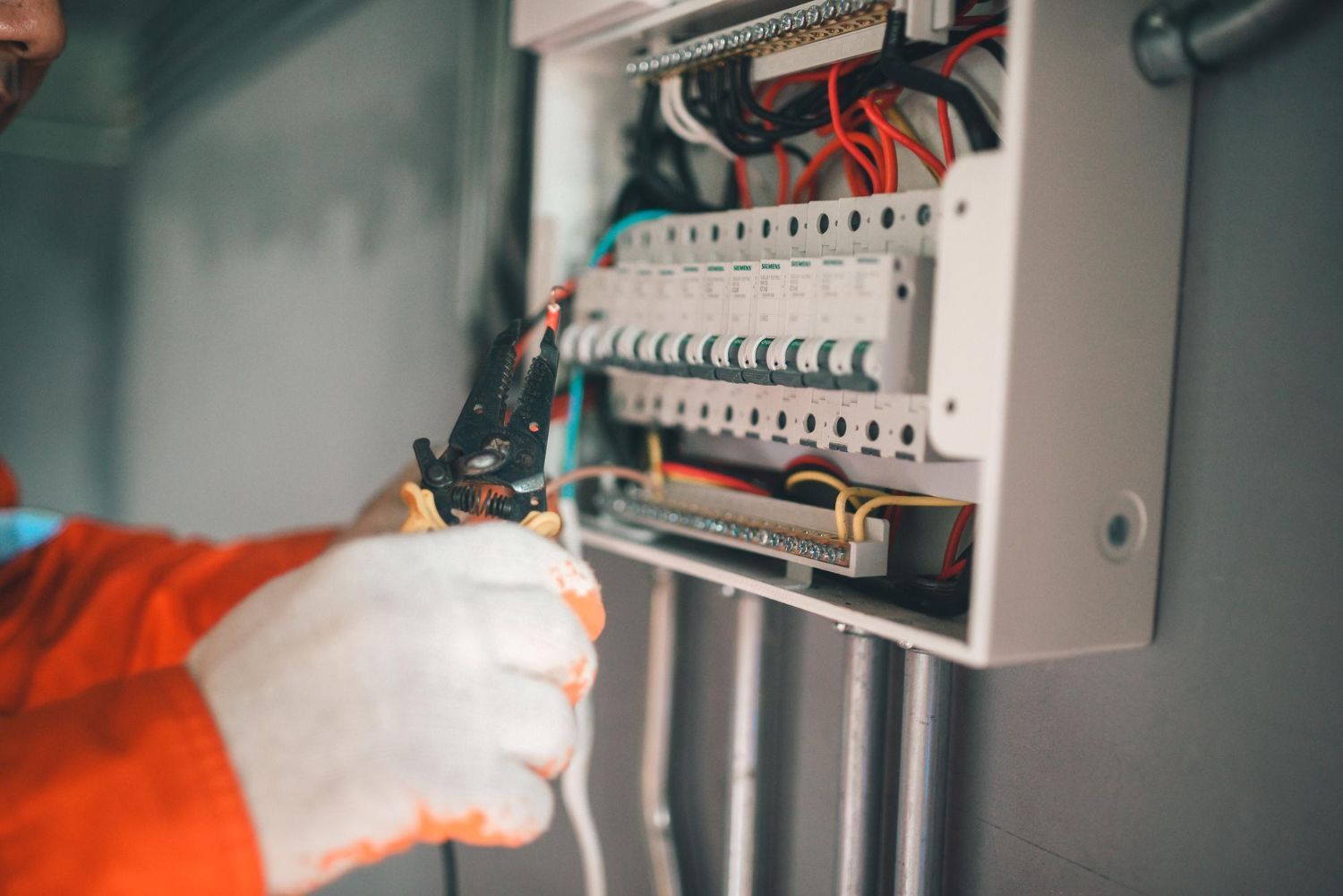 Electrician in orange suit working on a circuit breaker panel.