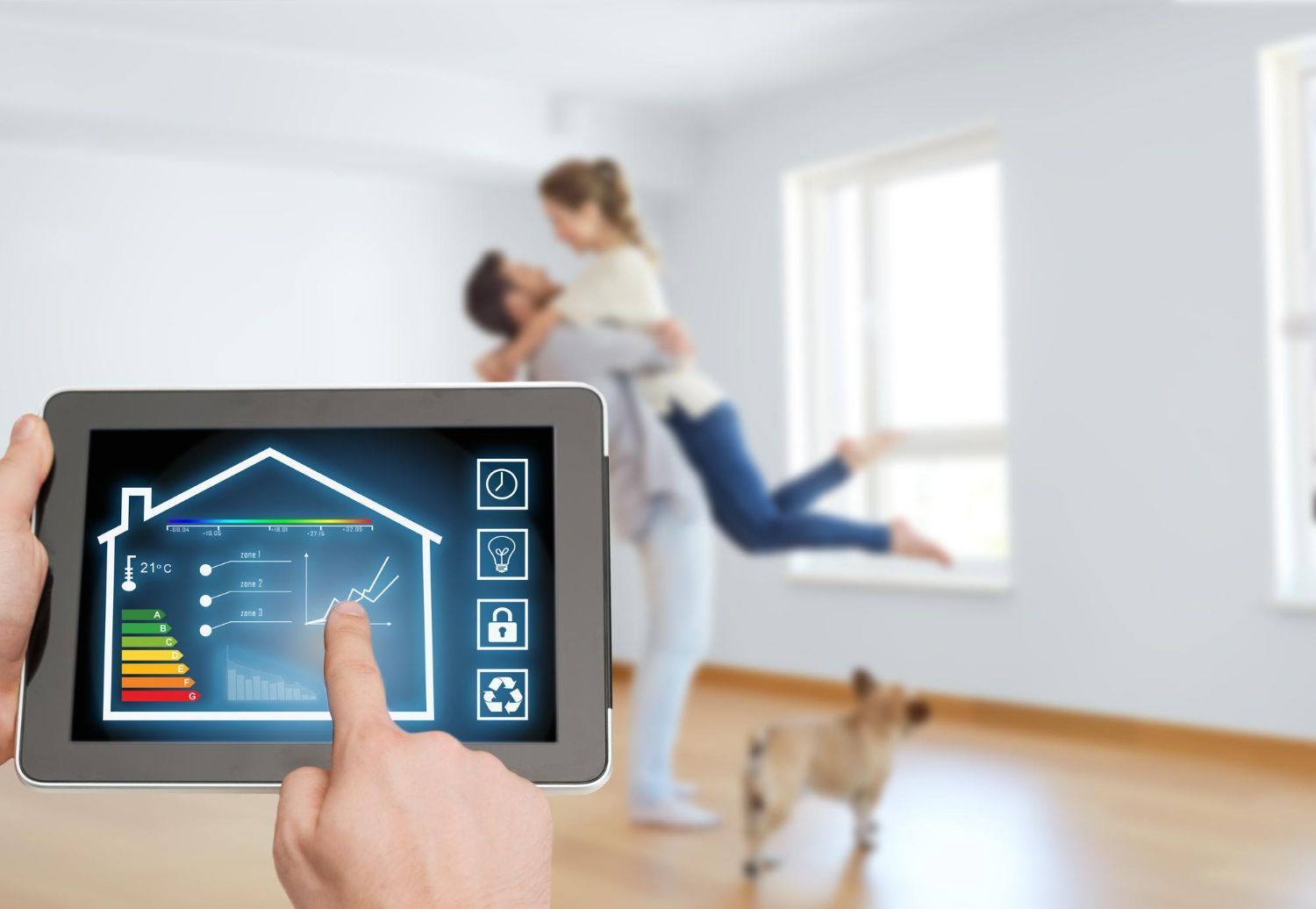 A person holding a tablet with a smart home interface. A couple is embracing in the background, with a dog nearby.