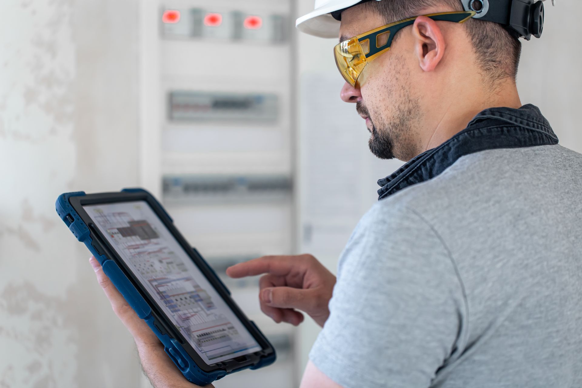 A man wearing a hard hat and goggles is using a tablet computer.
