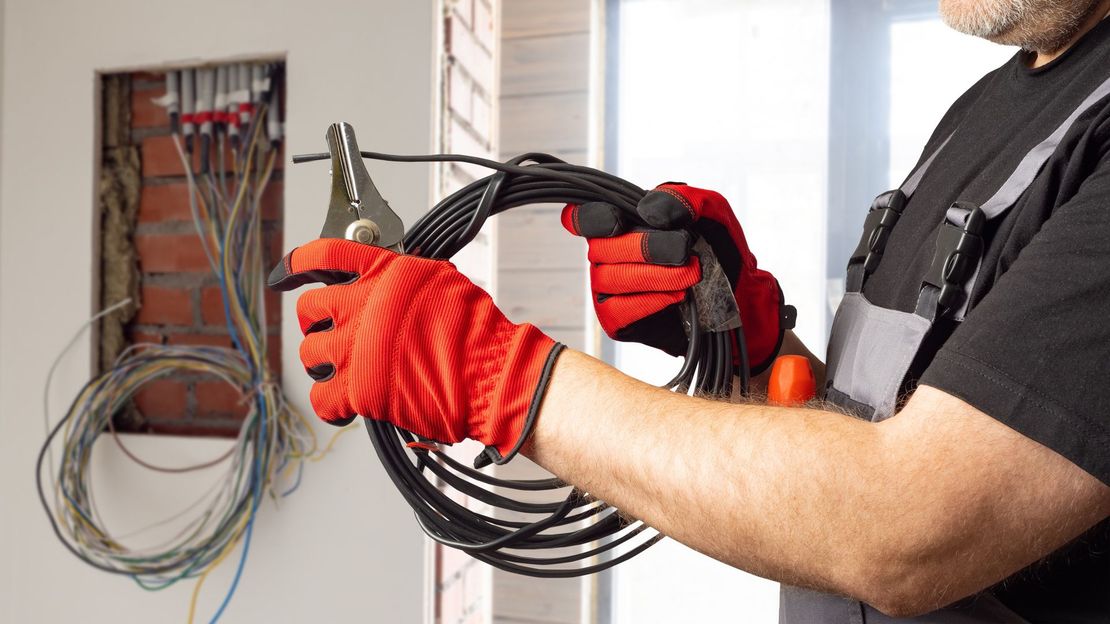 A man wearing red gloves is holding a wire and a pair of pliers.