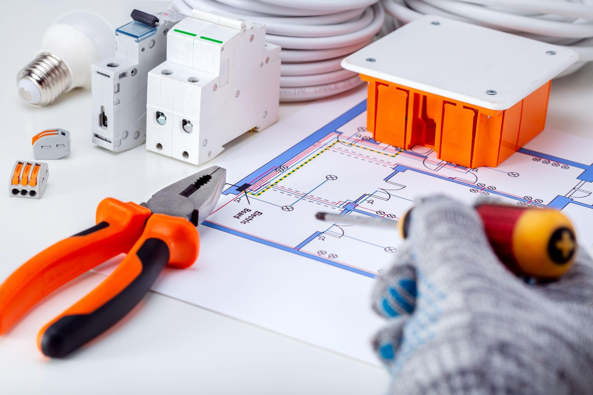 A person is holding a screwdriver over a blueprint of a house.