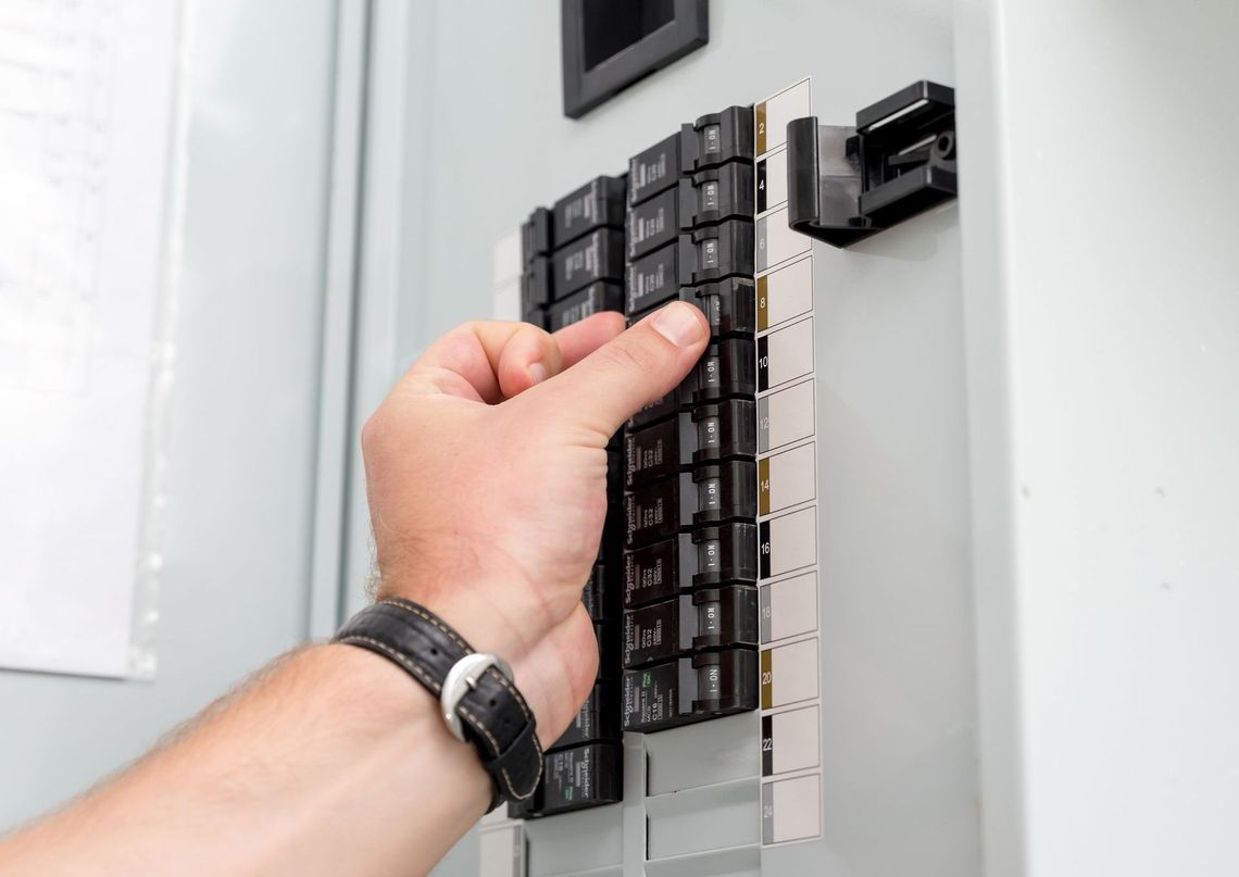 An electrician is working on an electrical box with a screwdriver.