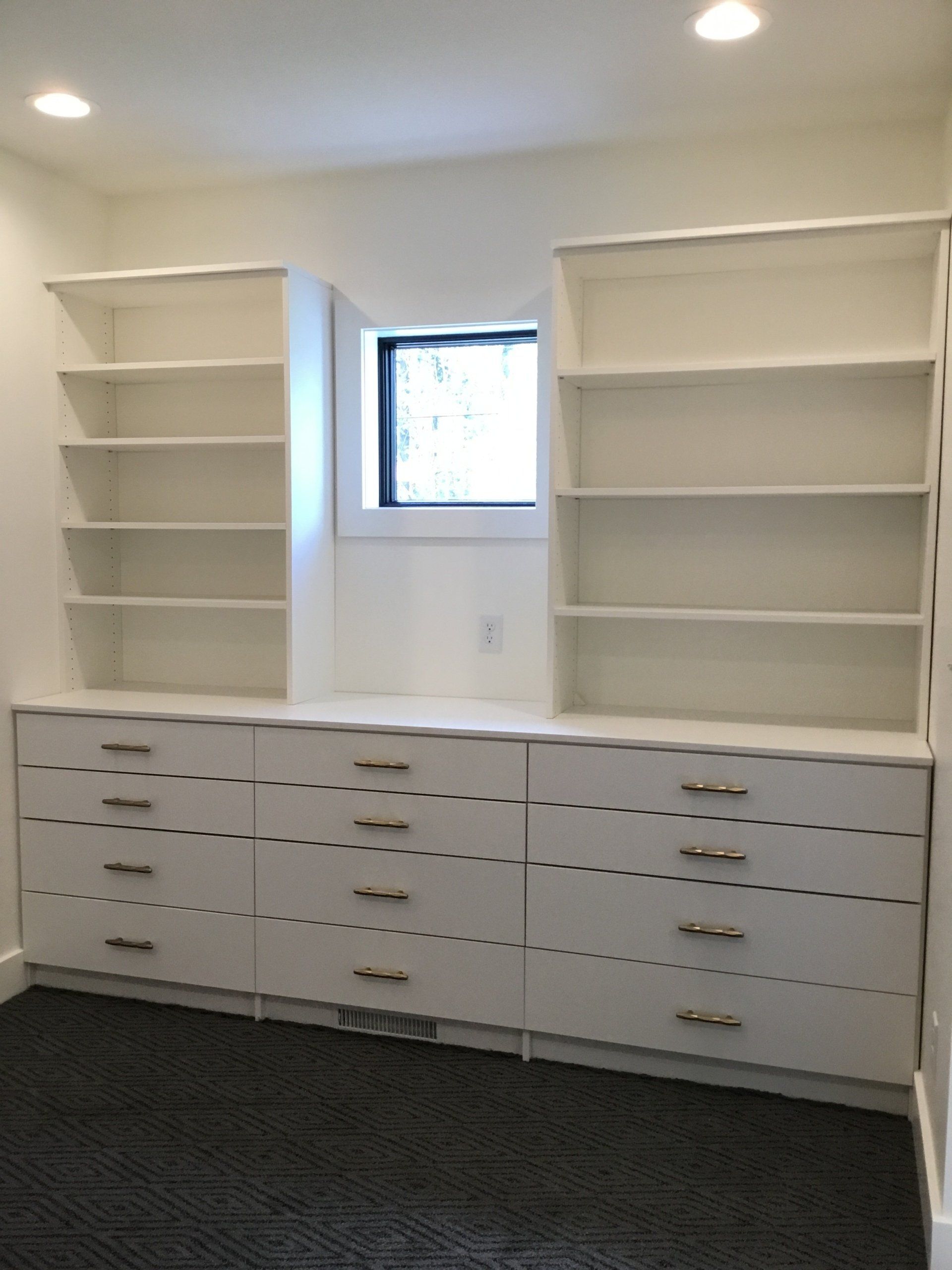 A room with white shelves and drawers and a window