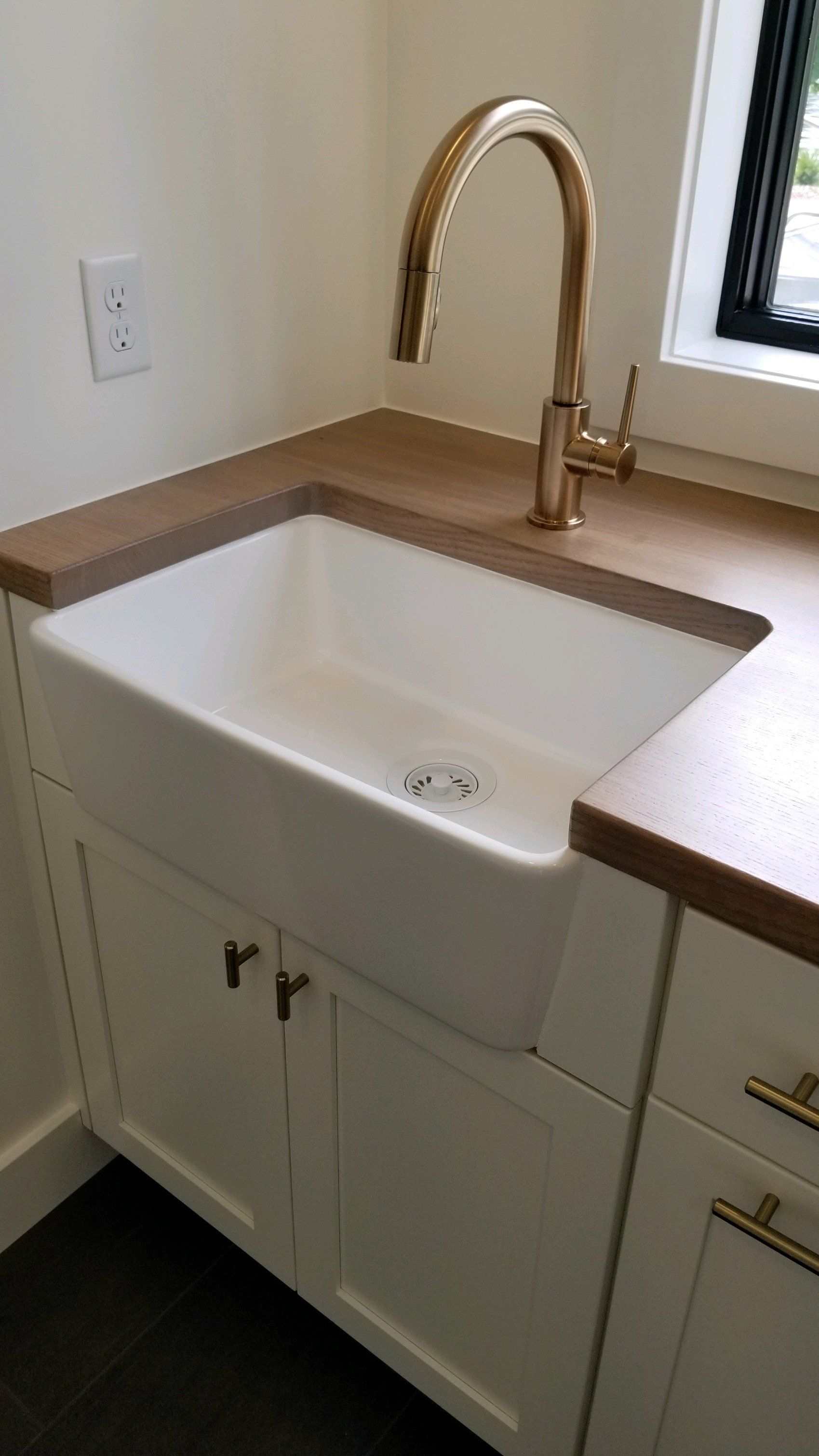 A kitchen sink with a gold faucet and a window in the background.