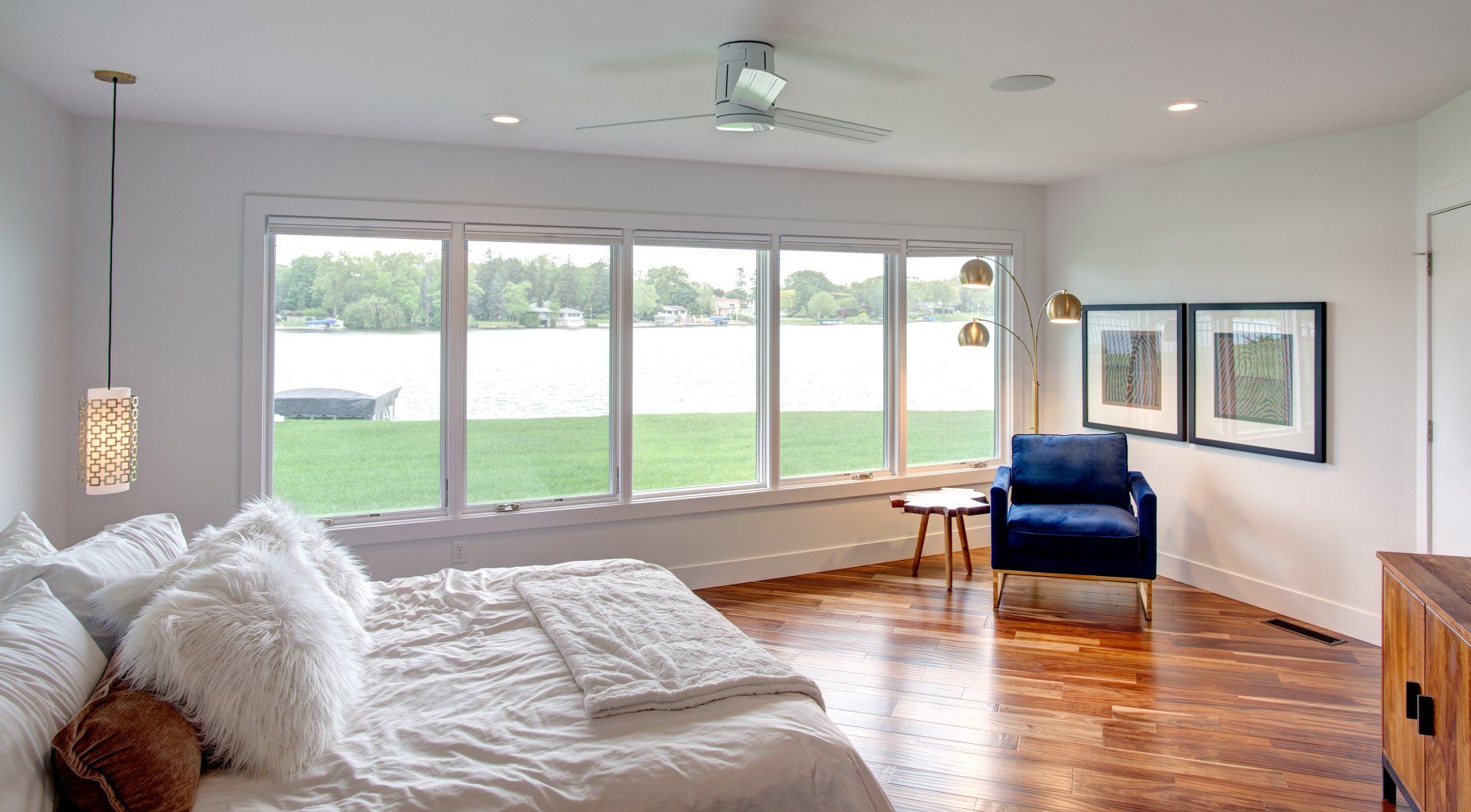 A bedroom with a large bed , chair , table and windows overlooking a lake.