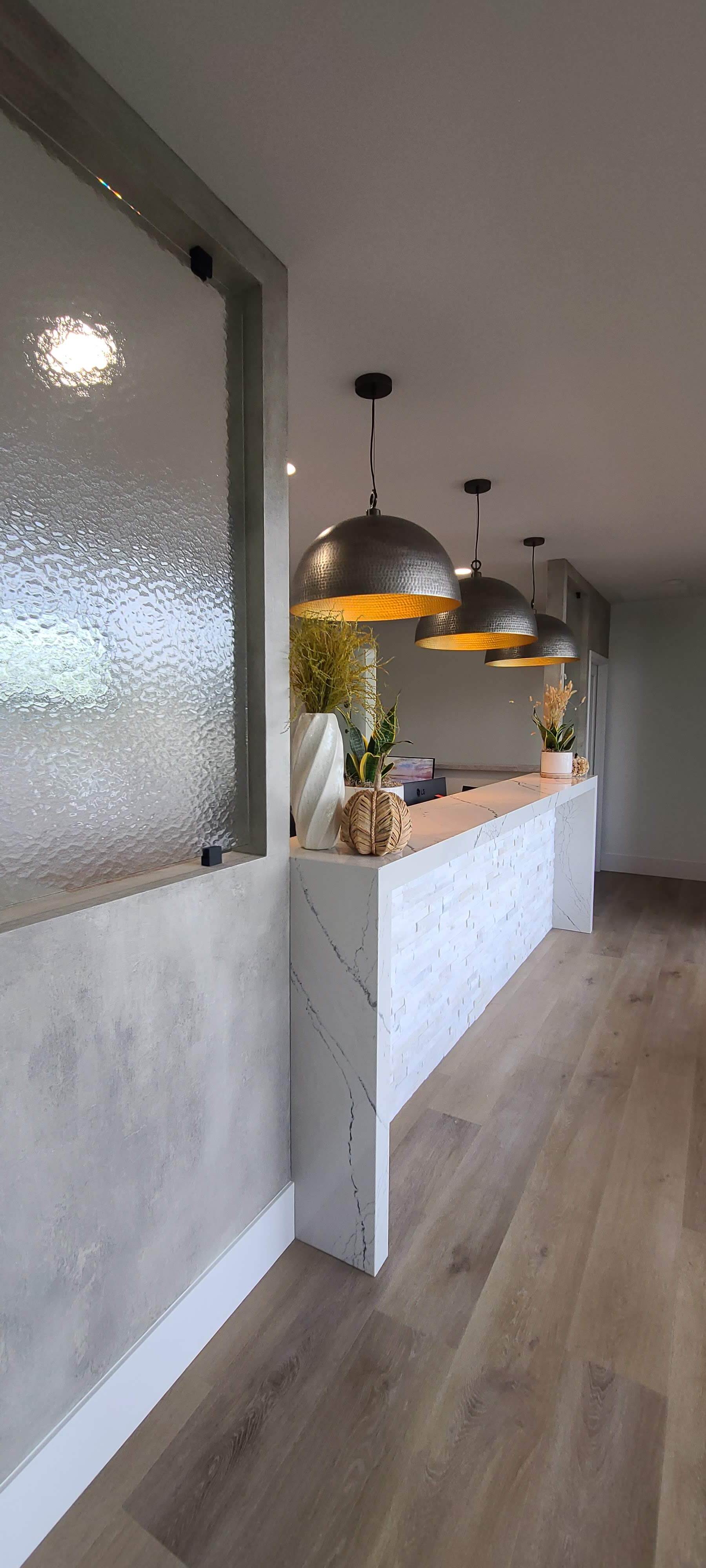 A long hallway with a counter in the middle of it and a row of lamps hanging from the ceiling.