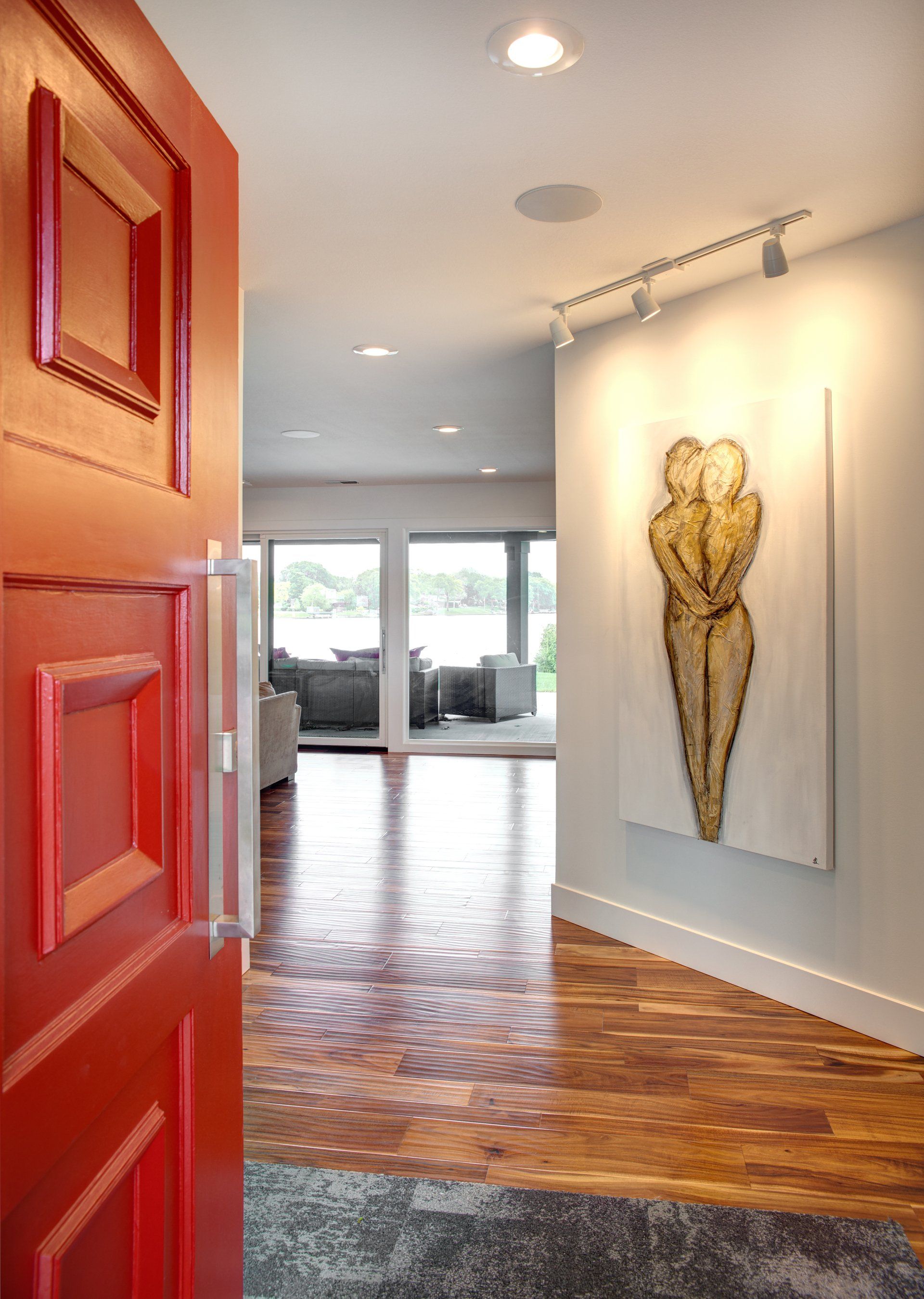 A red door is open to a hallway with a painting on the wall.
