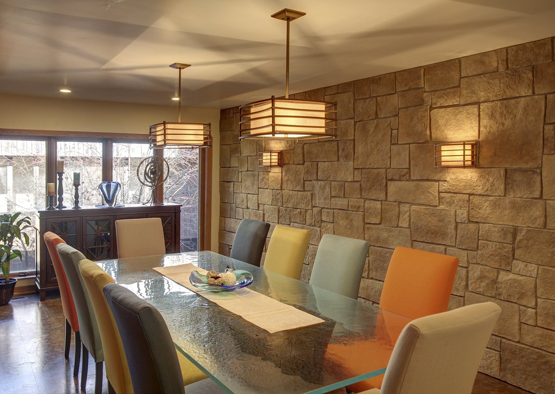 A dining room with a long glass table and colorful chairs
