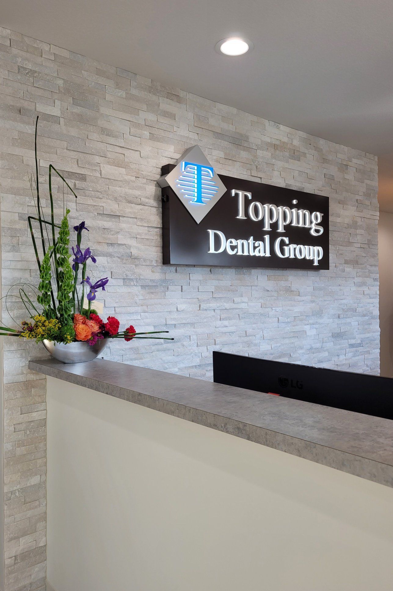 The front desk of a dental office with a sign above it that says topping dental group.