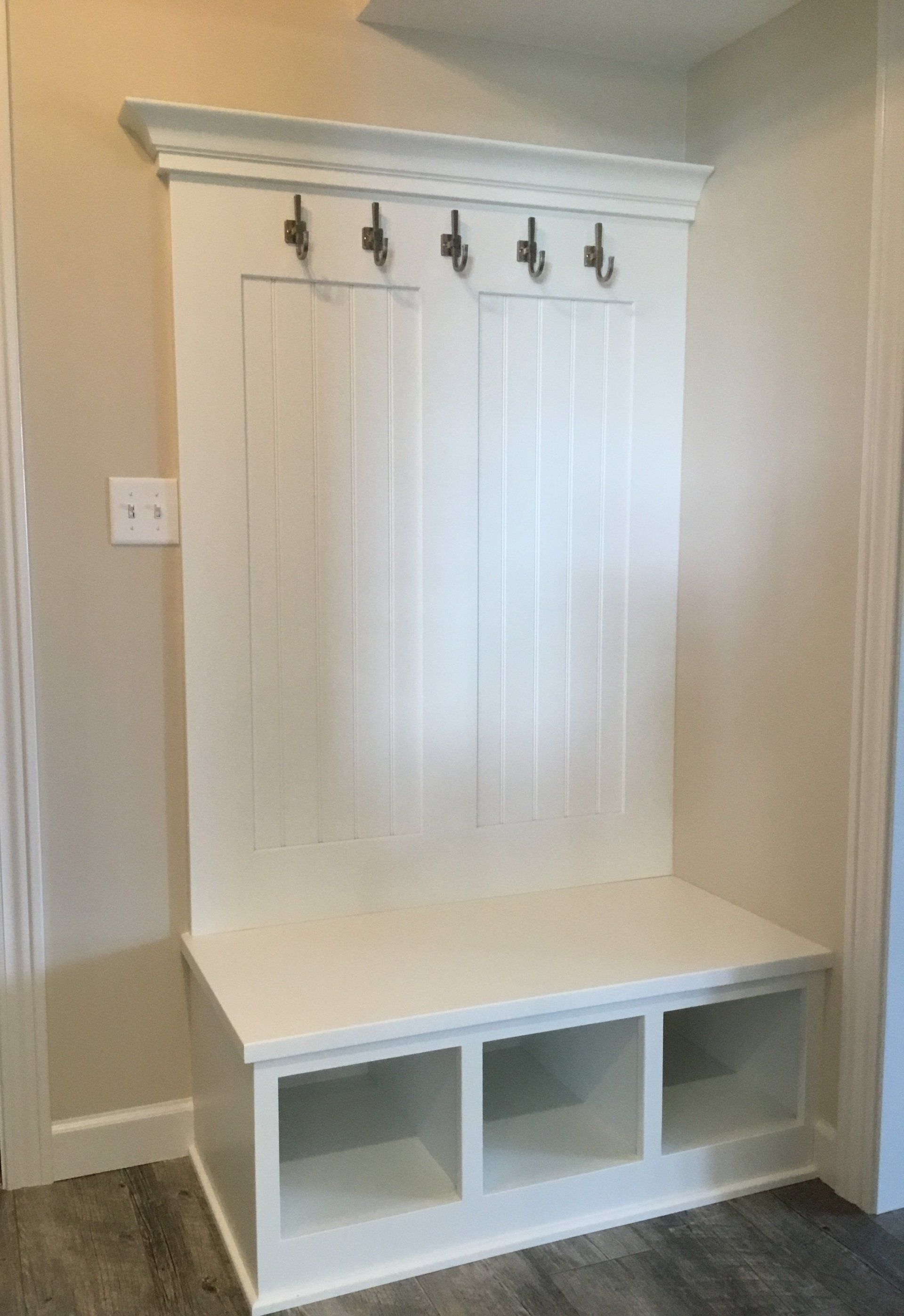 A white bench with shelves and hooks in a hallway.