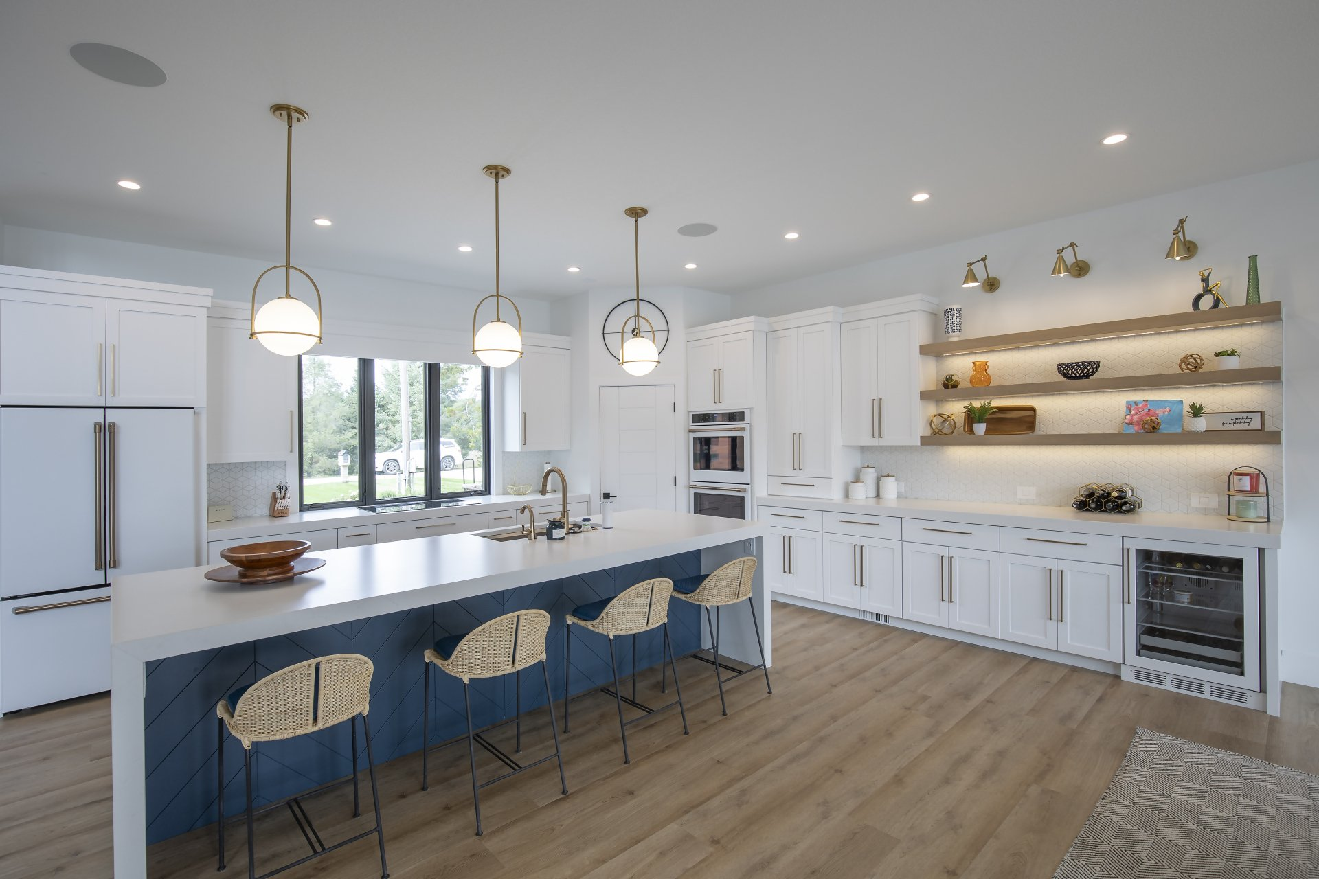 A kitchen with white cabinets , a large island , stools and a refrigerator.