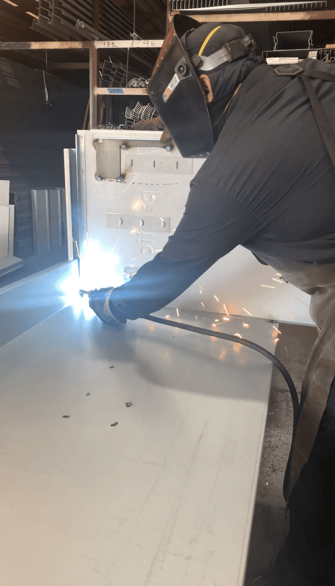 Welder in a protective mask and apron welds metal. Sparks fly in a workshop setting.