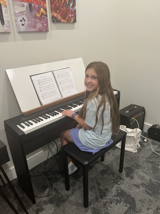 A young girl is playing a piano in a room.