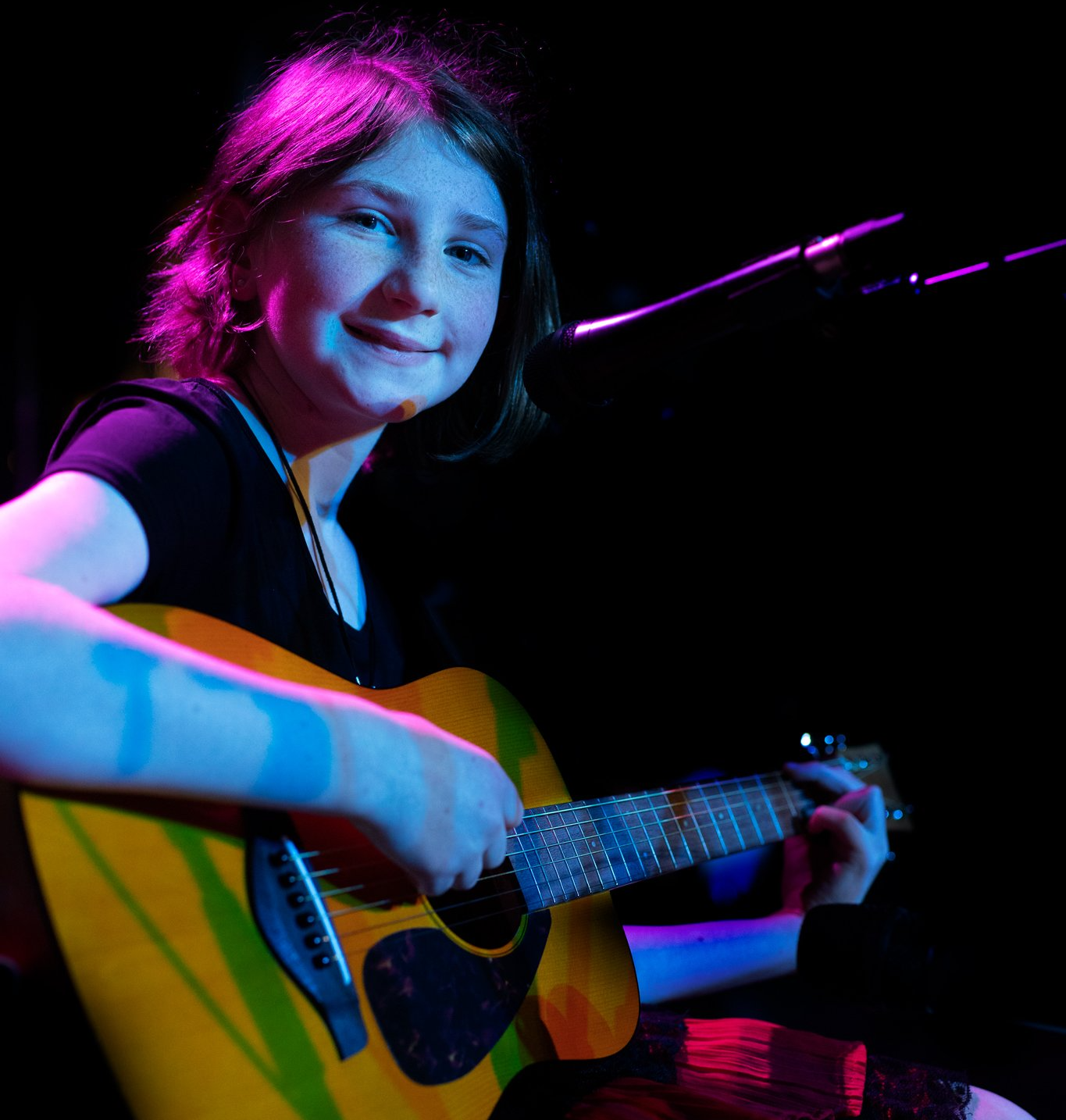 A young girl is playing a guitar on stage