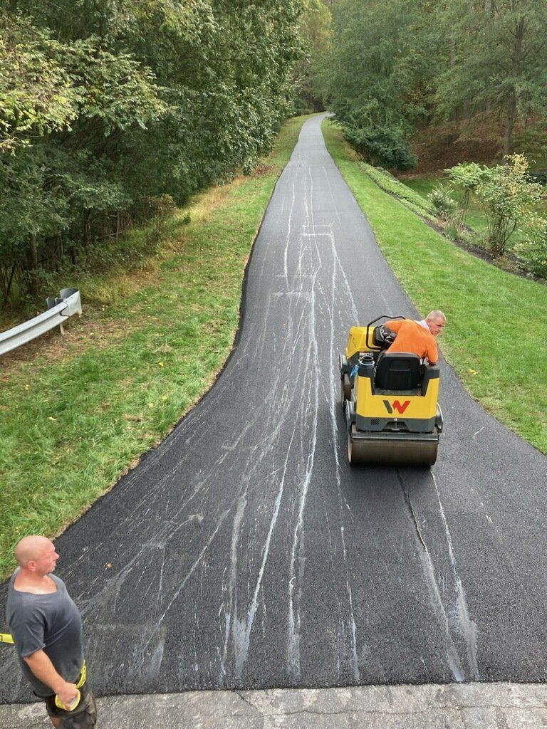 A man is standing on the side of a road while a roller is going down it