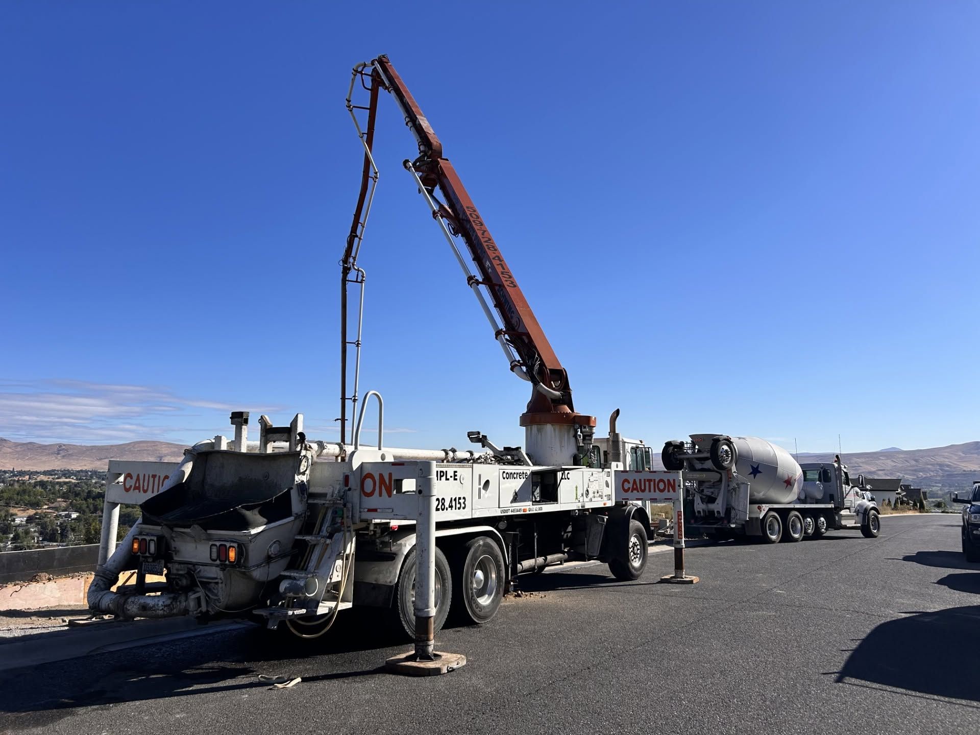 Concrete mixer truck with extended boom pumping concrete at a construction site under a clear blue sky