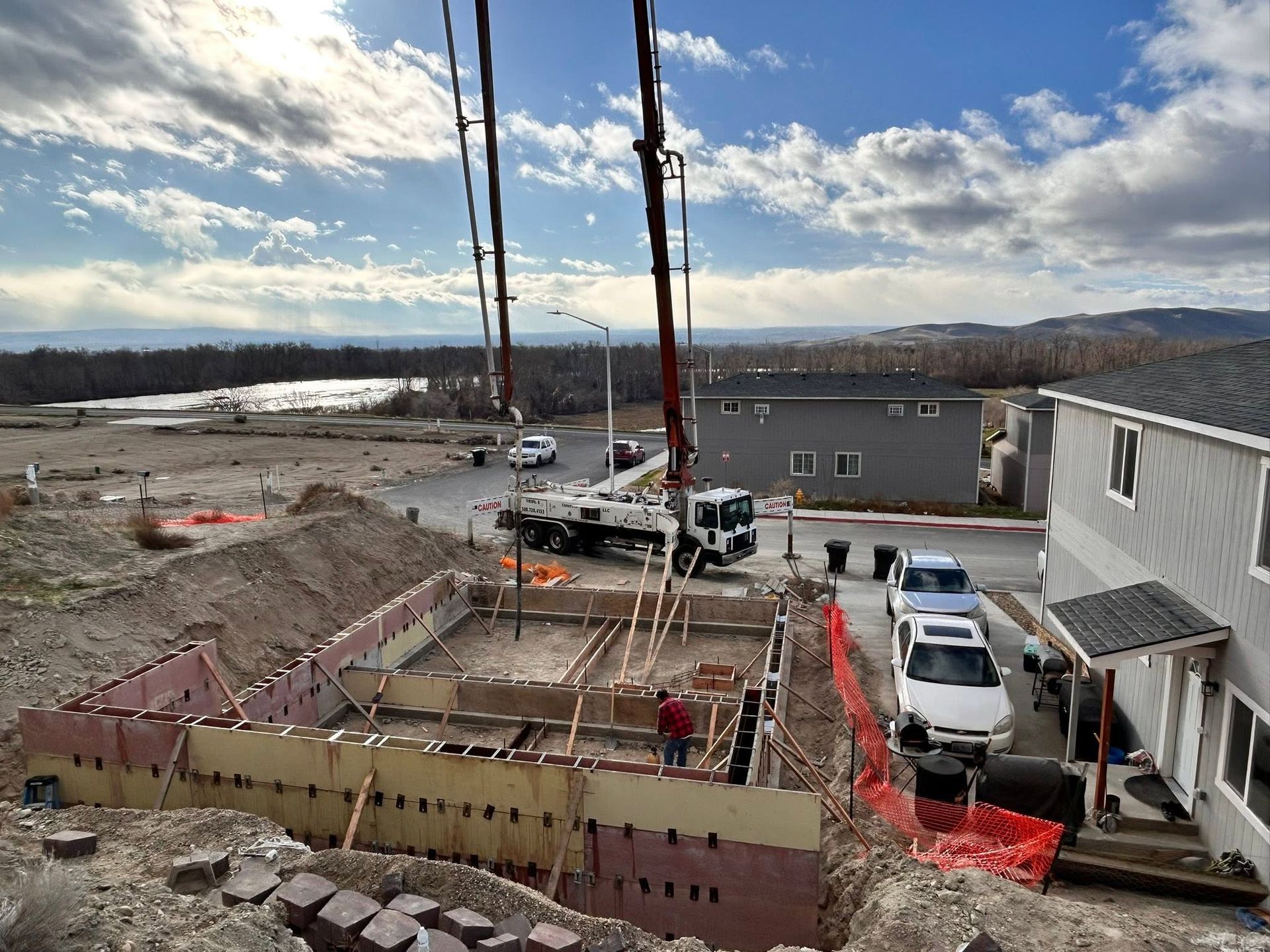 Construction site with concrete forms, trucks, and a building under a cloudy sky