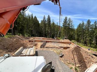 Construction site with gravel, timber, and excavator arm in a forested area