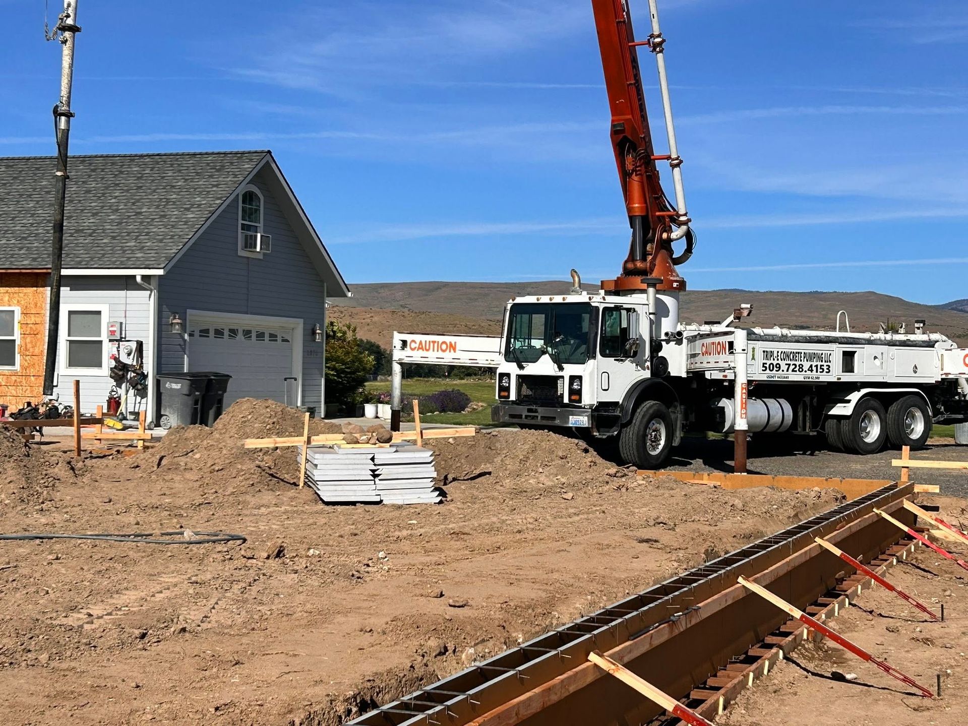 Construction site with crane truck pouring concrete foundation near houses on a clear day