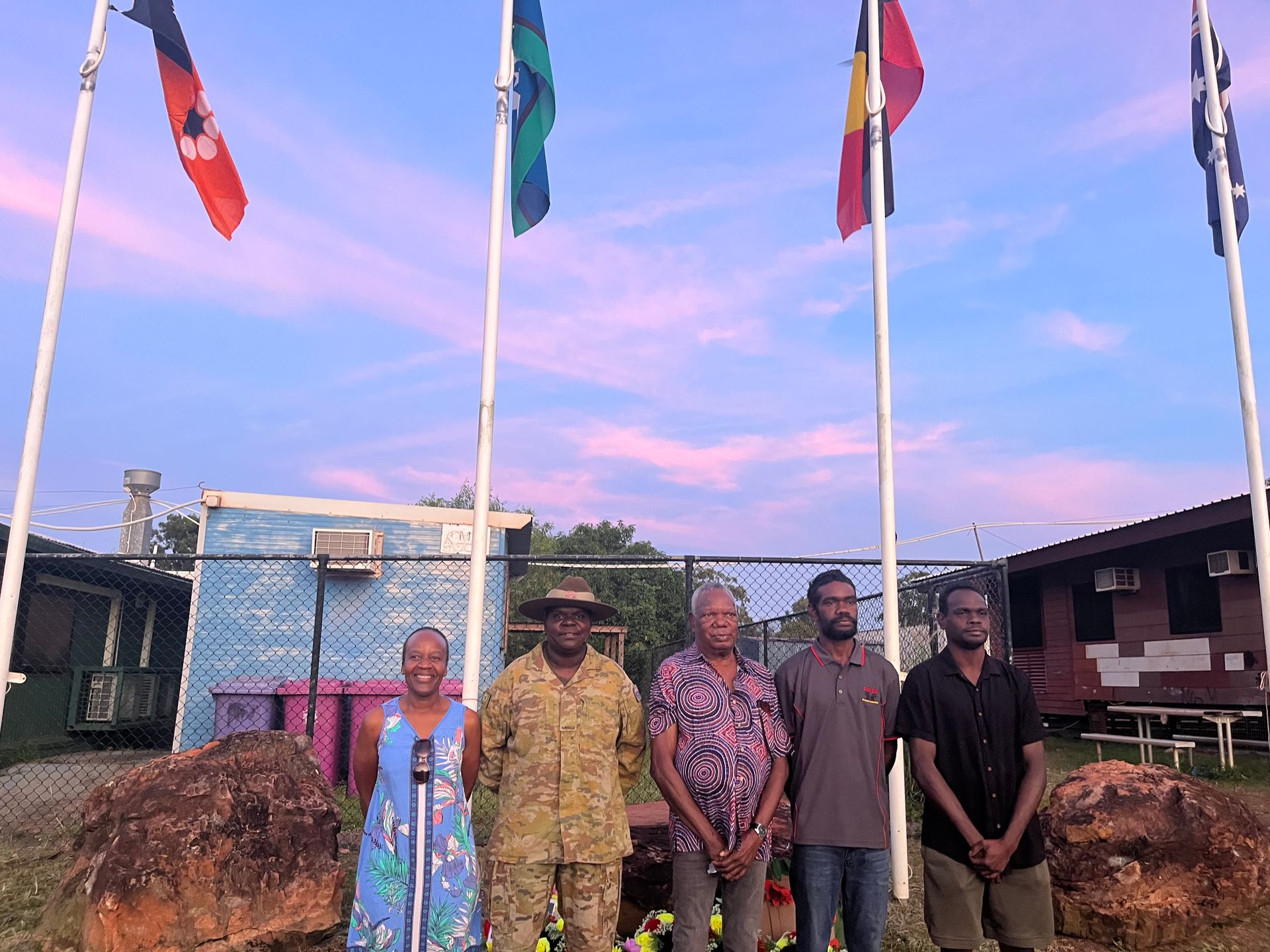A group of five people standing together in front of four flags.
