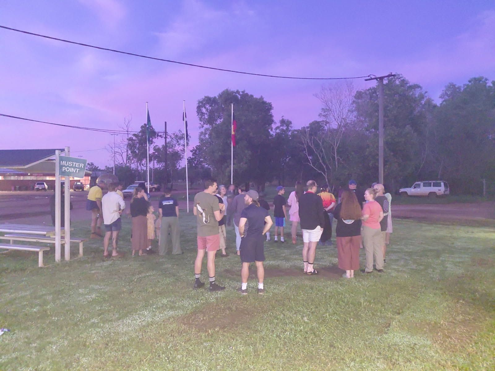 A group of people standing together at dawn. Four flag poles are in the background. 