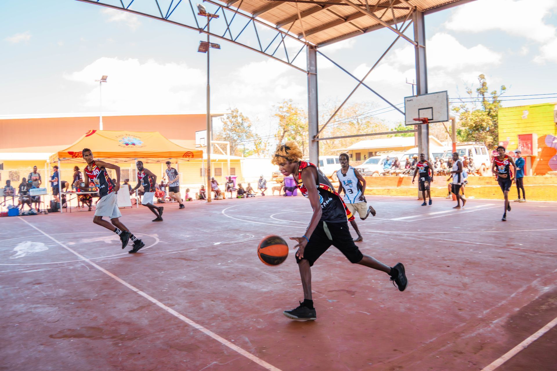 An outdoor basketball court with one player dribbling the ball.