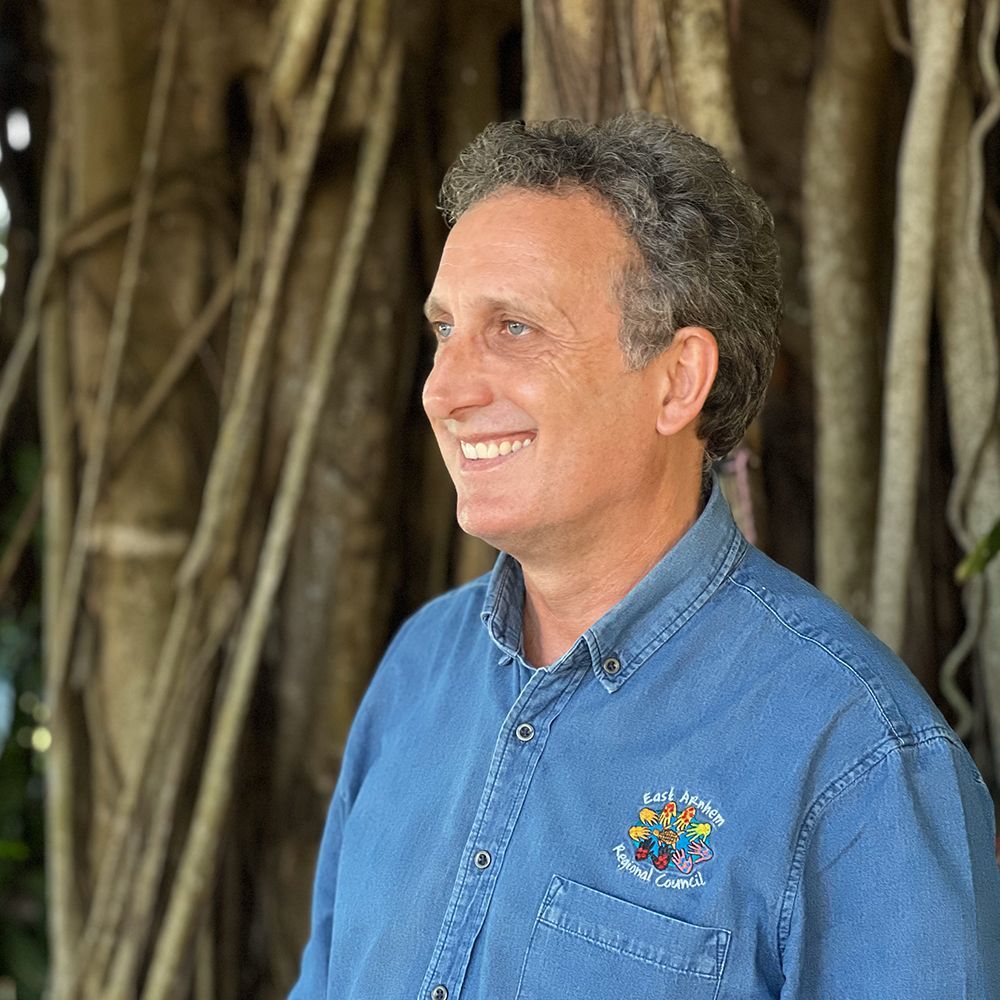 A man wearing a blue shirt. He is smiling and looking to the left of the camera.