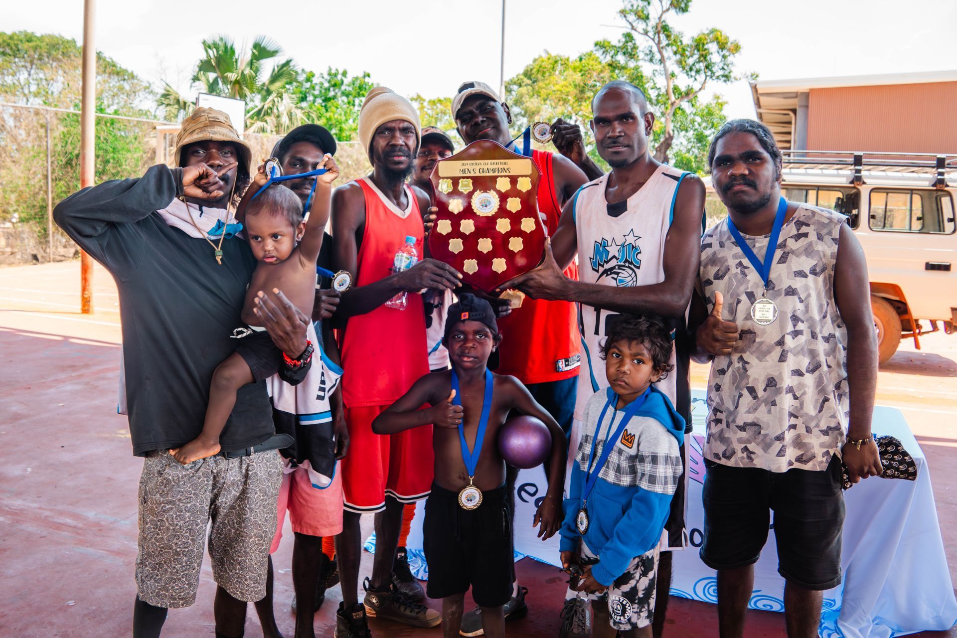A group of people gather together. The person in the middle holds a trophy
