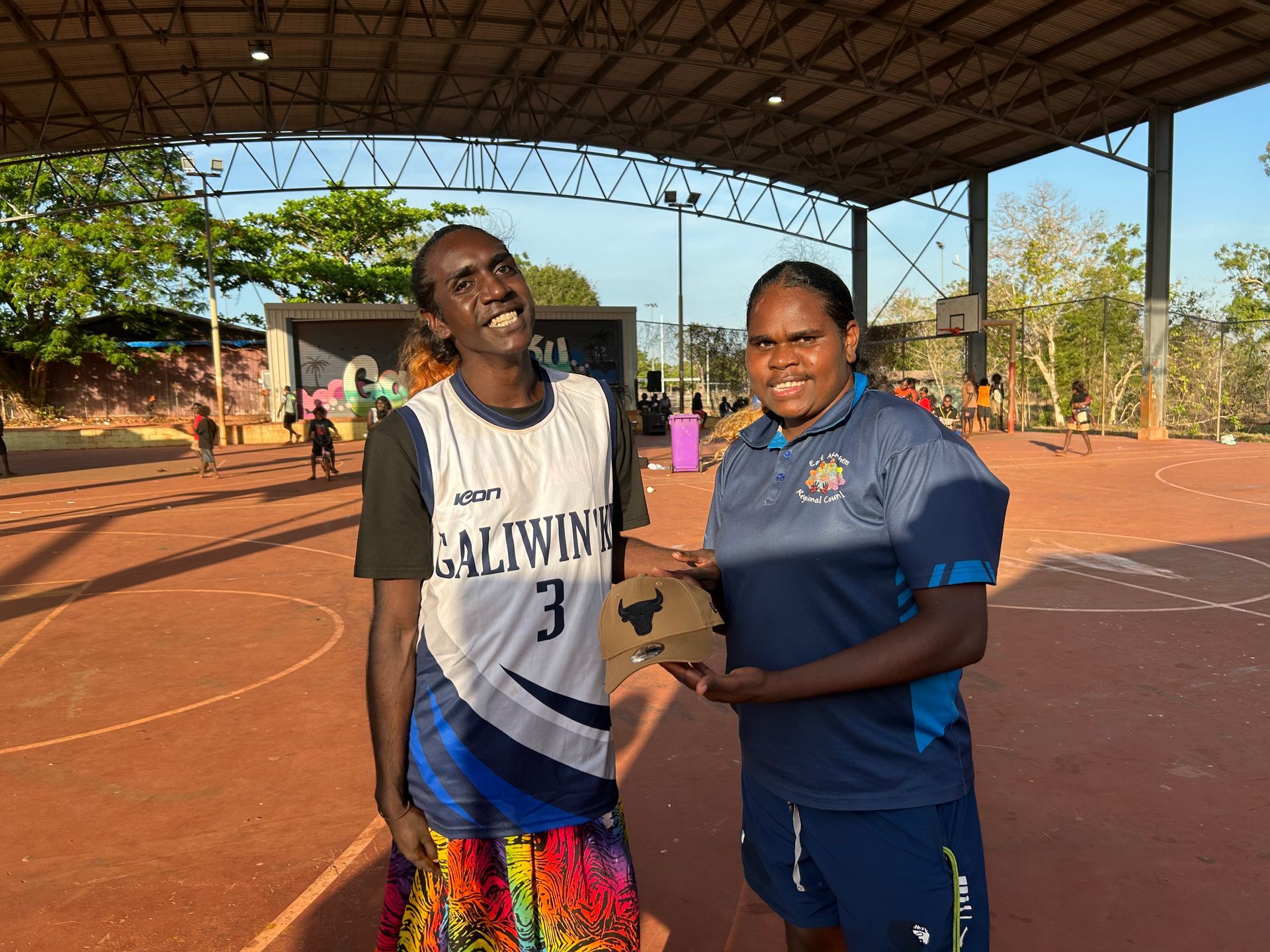 Two people stand together. One is giving the other a cap.