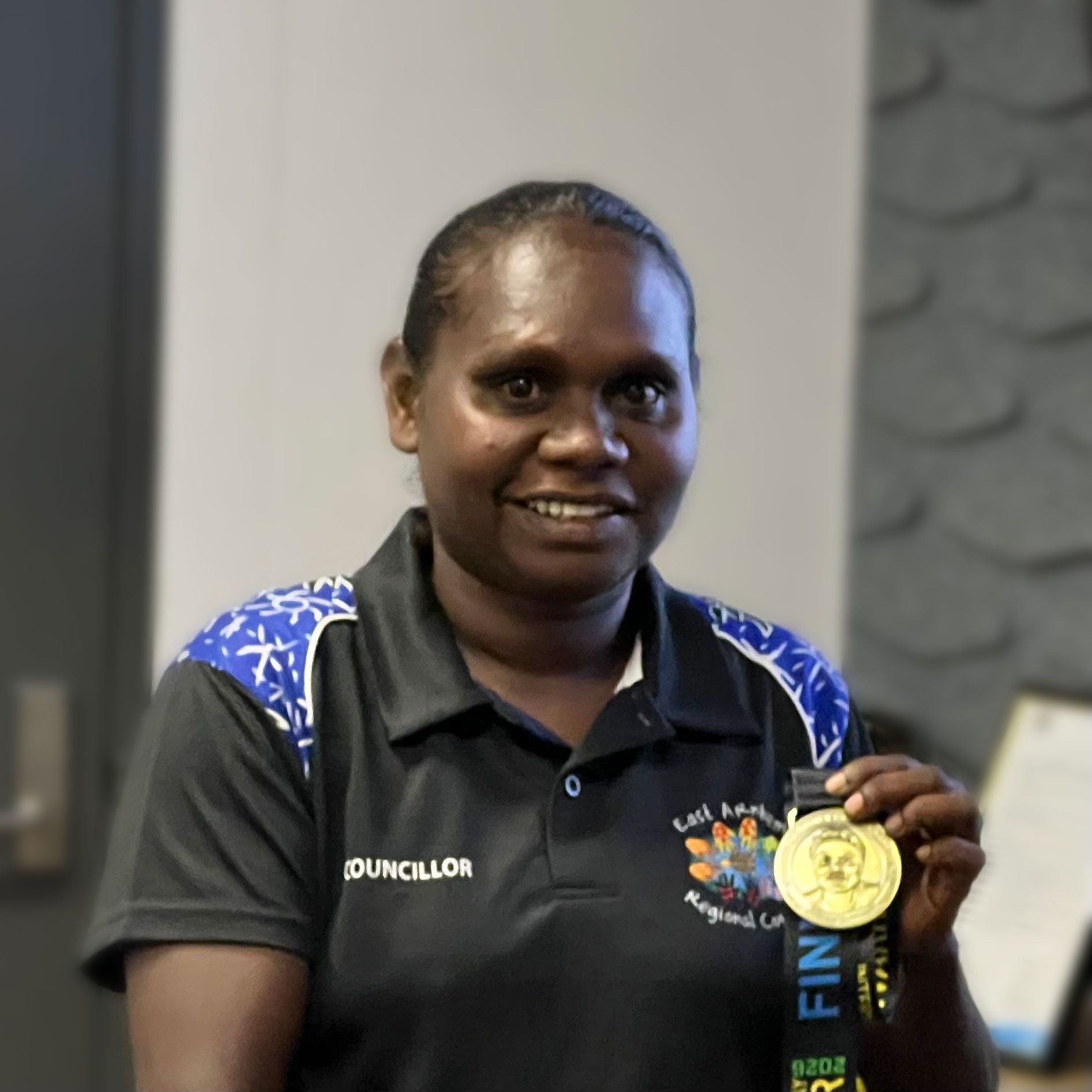 A woman smiles and holds a gold medal in her left hand