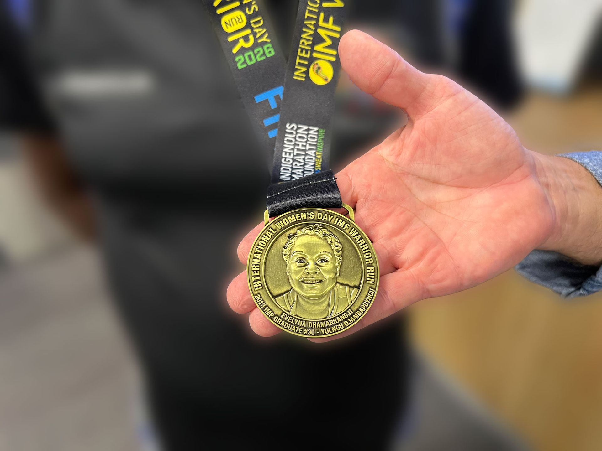 A gold medal with a woman's face in the centre. Around the boarder are the words 'International Women’s Day IMF Warrior Run'