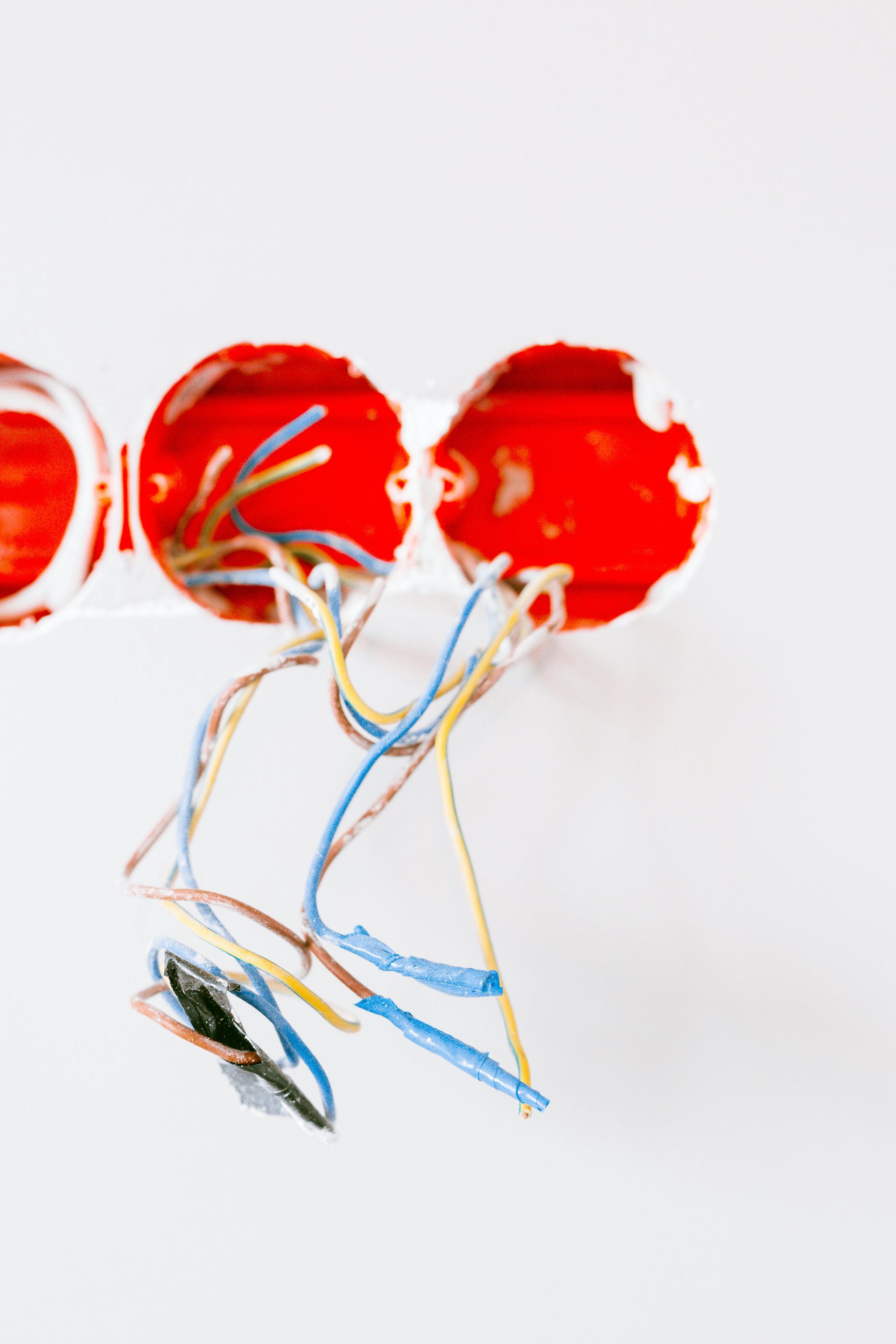 Three red electrical wall boxes with exposed wires hanging against a plain white wall.